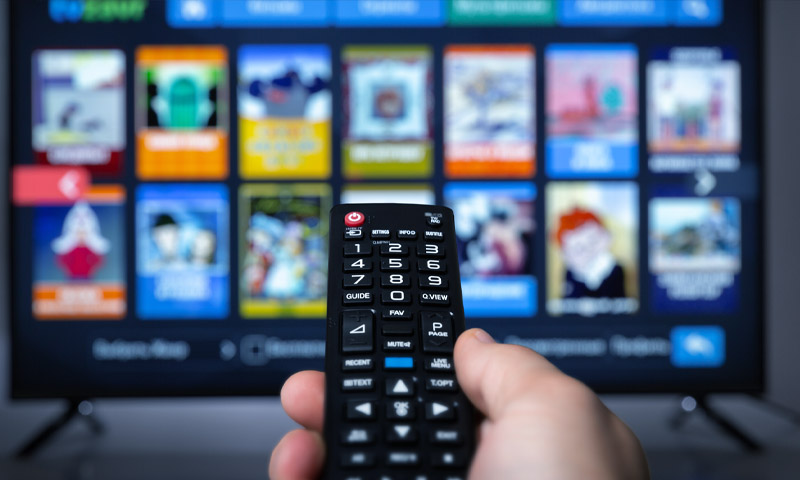 hand holding TV remote control in front of TV