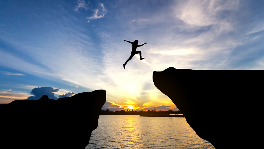 person jumping the gap to a higher platform in front of sunset sky
