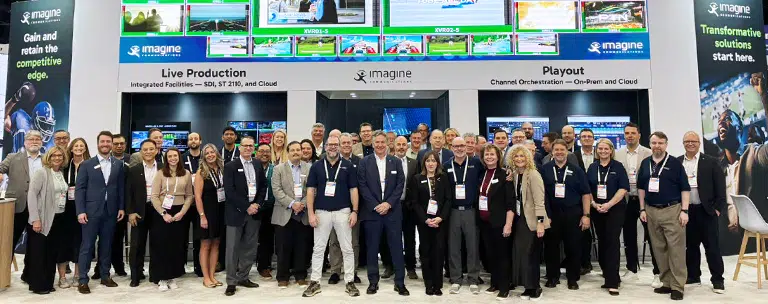 group photo of the Imagine Communications' team that attended NAB 2026 standing in front of our booth with the large overhead multiviewer screen